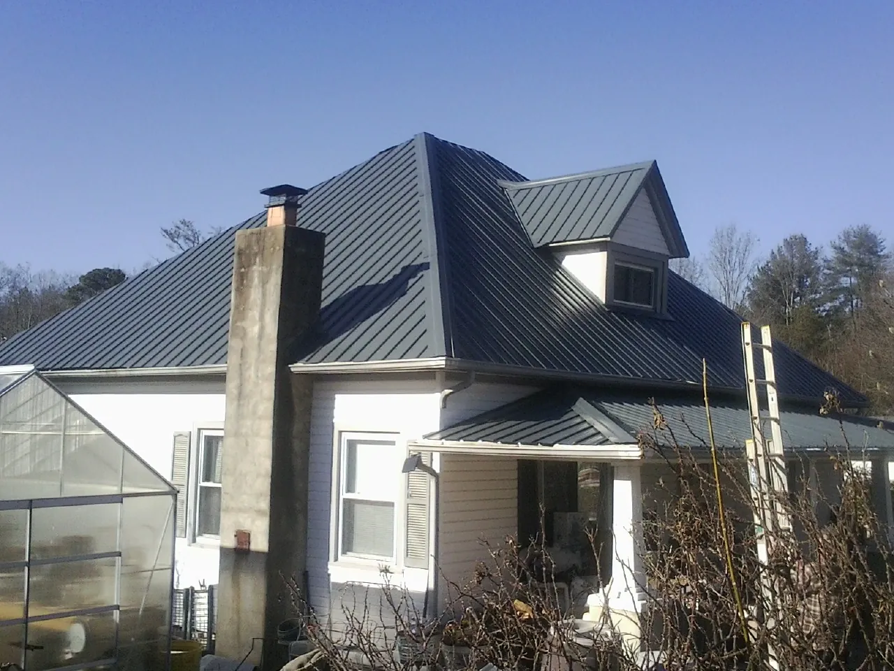 Dark blue standing seam metal roof on a white farmhouse with dormer — Slate & Tile Roof Repair by Roofing Brothers in Brandt