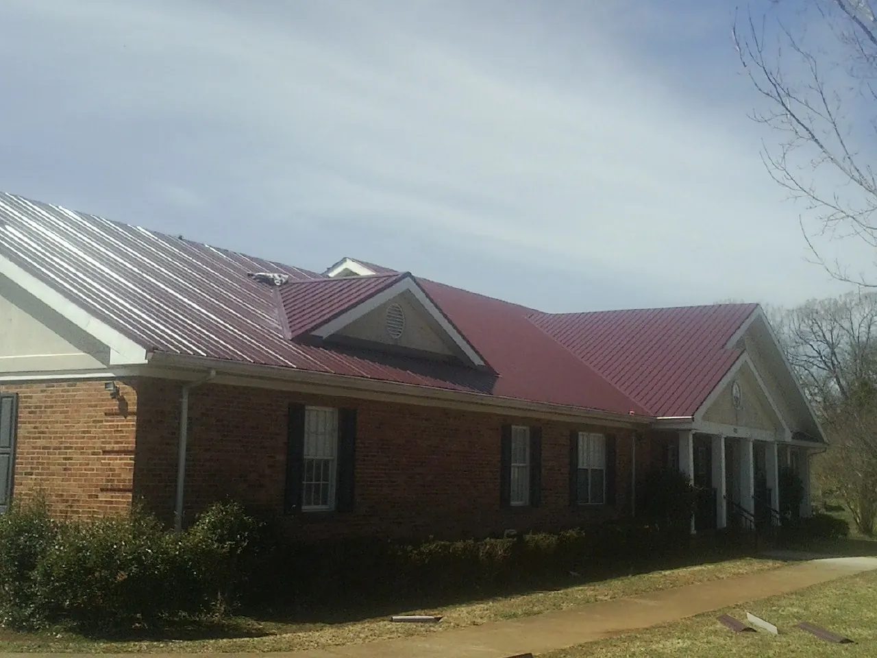 Red metal roof with gabled entries on a long brick building, from a Hail Damage Roof Repair job in Brandt