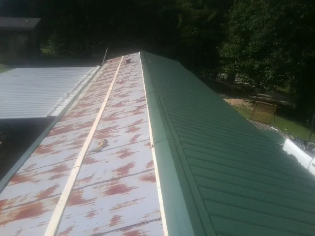 Old rusted panels beside newly installed green metal roofing — Wind Damage Roof Repair by Roofing Brothers in Brandt