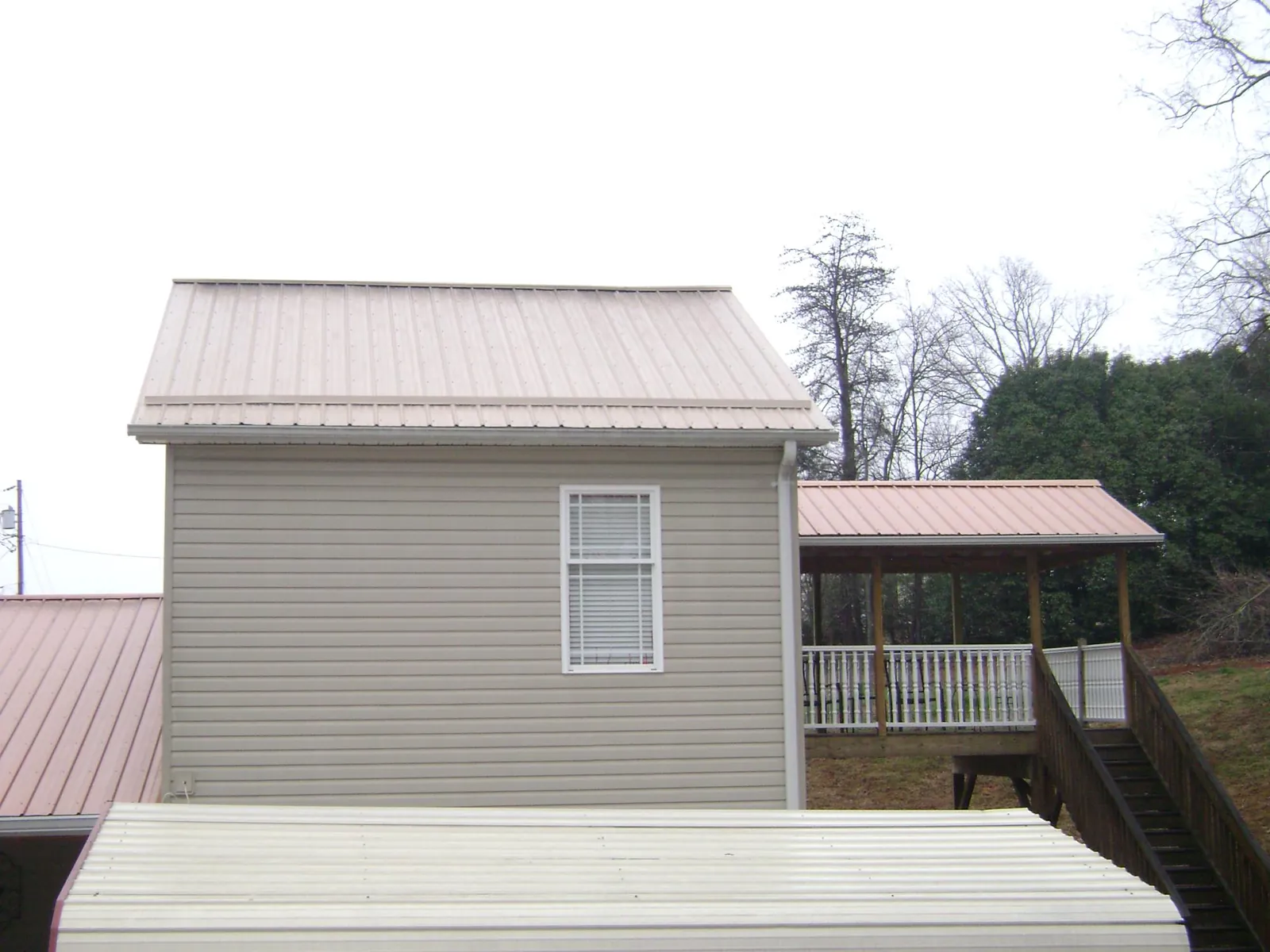 Tan metal roofs on a two story addition and attached porch, from a Roof Replacement job in Brandt